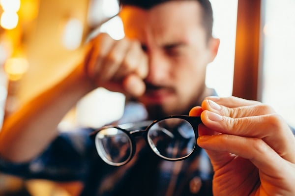Man holding his glasses so he can rub his eyes because of dry eye symptoms