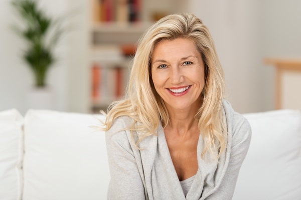 Middle aged woman with blonde flowing hair facing the camera and smiling indoors