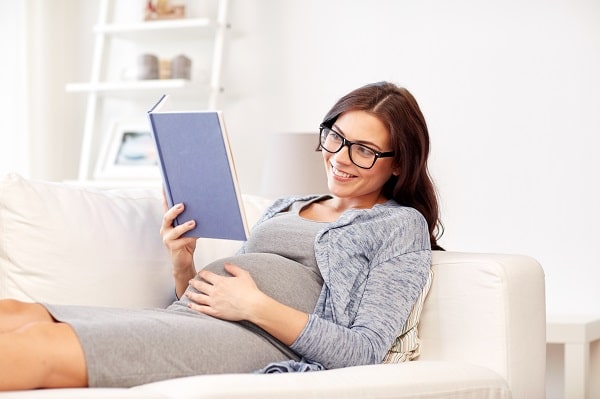 Pregnant Alabama woman reading a book with glasses on a couch